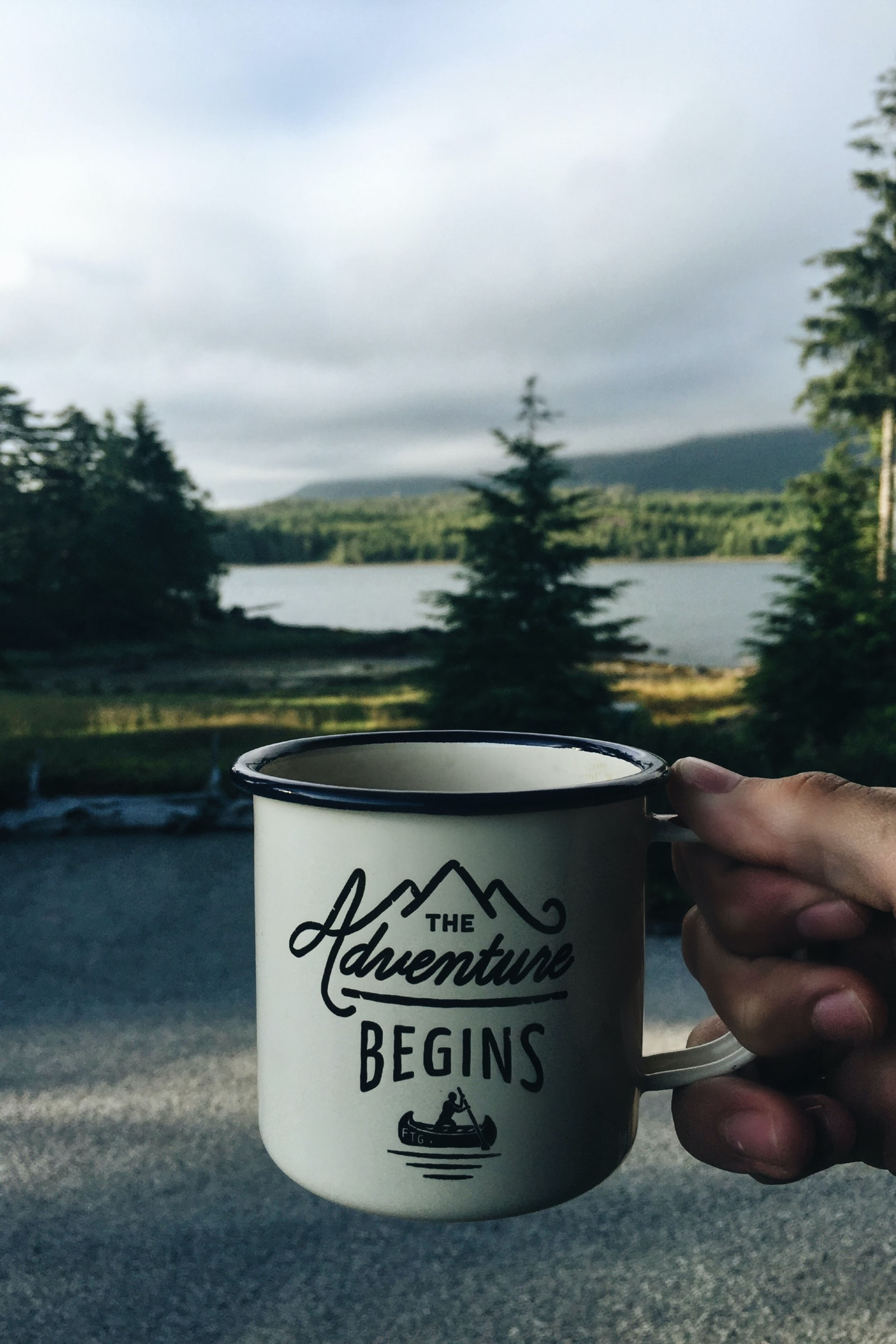 Person camper holding coffee mug that has The Adventure Begins embossed beautiful canadian forest