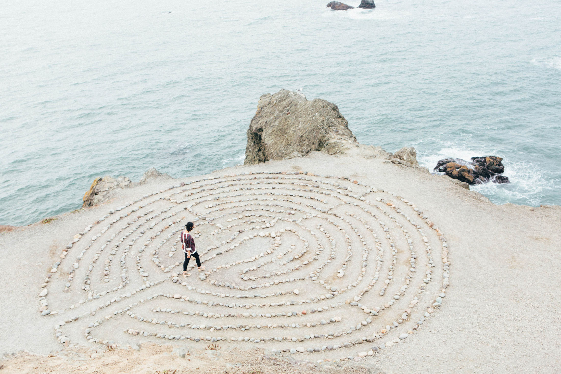 Woman near the ocean walking through a maze made of large rocks